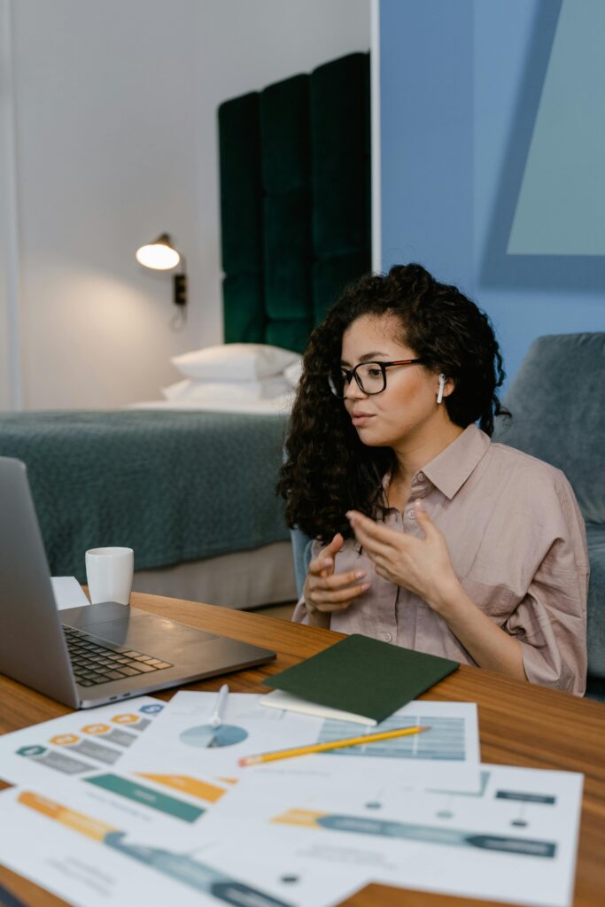 Young woman participating in an online meeting from her home office, with charts and laptop.